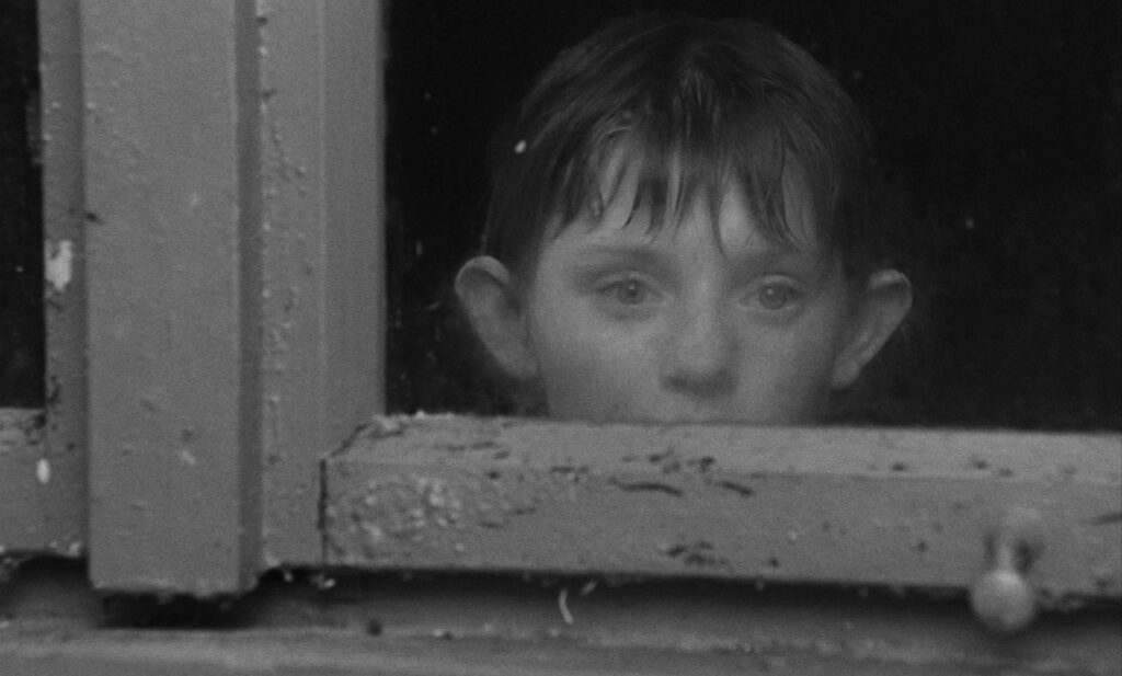 Black and white photo of a child's head, looking out a windown